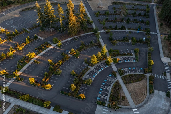 Fototapeta Aerial drone photo of an empty parking lot in Oregon City with landscaped rows, trees showing fall colors, and golden sunset light creating long shadows across the pavement and walkways