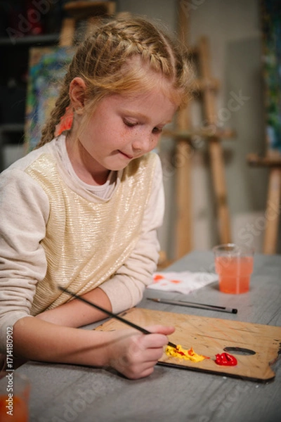 Fototapeta Girl enjoys painting in a workshop. Children drew a picture in art class. Art lesson. Girl mixed and combined colors. Education and learning concept. School kid drawing with brush on easel. Closeup.