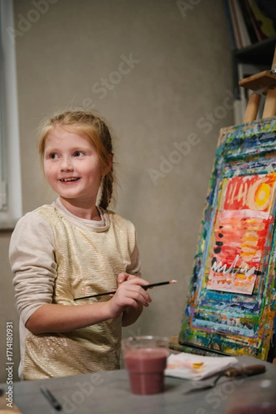 Fototapeta School kid drawing with brush landscapes on easel. Mix and combine colors. Child drew a picture in art class. Girl enjoys painting in a workshop. Art lesson. Education and learning concept.