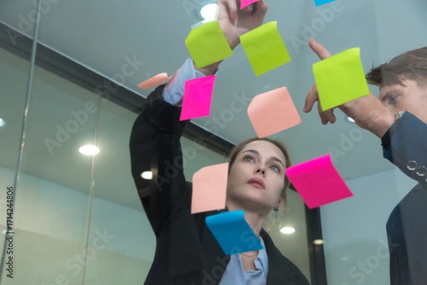 Fototapeta Creative professionals collaborate in modern office, using colorful sticky notes for brainstorming and planning. Their focused expressions reflect teamwork and innovation.