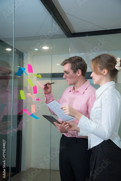Fototapeta Creative professionals collaborate in modern office, using colorful sticky notes for brainstorming and planning. Their focused expressions reflect teamwork and innovation.