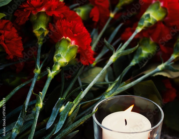 Obraz A memorial candle and red carnations. A symbol of remembrance and grief.
