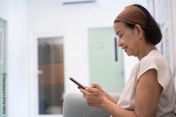 Obraz Happy senior woman smiling, using smartphone indoors, concept of elderly technology, online lifestyle, digital communication, healthcare support, modern aging, independent living with mobile devices.