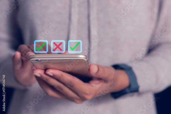 Fototapeta Close-up of hands holding smartphone with glowing check and cross icons, symbolizing digital decision making, online voting and mobile application.
