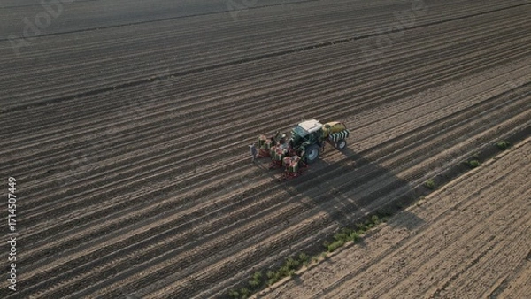 Fototapeta A modern tractor with agricultural equipment works across a vast plowed field creating perfect rows under a bright sky indicating a new growing season