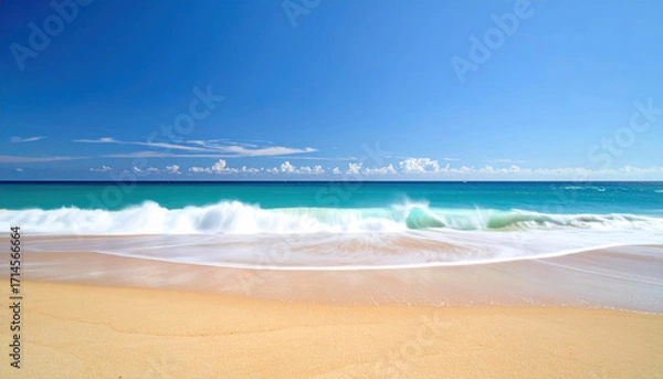 Fototapeta Ocean wave crashing on sandy beach with clear blue sky and distant clouds creating peaceful and refreshing coastal scene under bright sunlight
