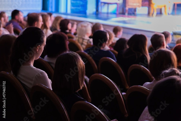 Fototapeta The audience in the theater watching a play. The audience in the hall: adults and children.