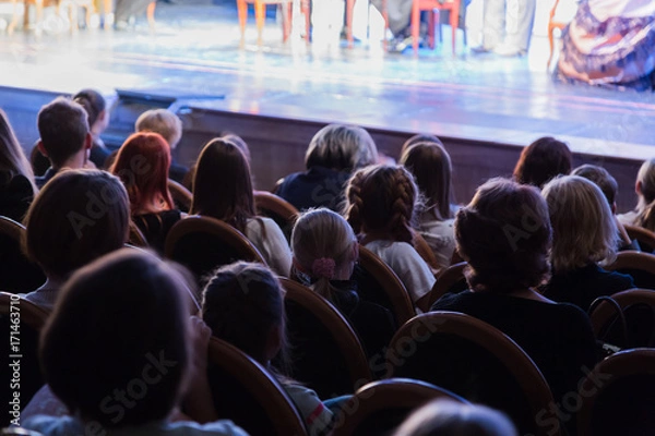 Fototapeta The audience in the theater watching a play. The audience in the hall: adults and children.
