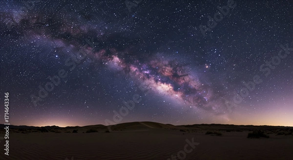 Fototapeta The Milky Way galaxy arcs majestically across a star-filled night sky above a serene desert landscape with rolling dunes.