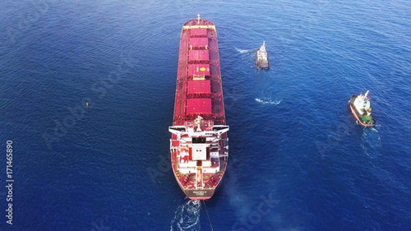 Obraz Large bulk carrier ship pulled by tugboats in open water