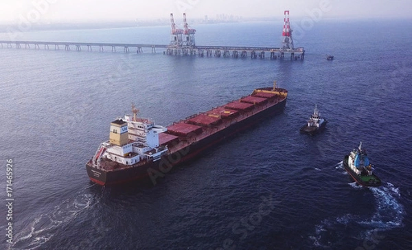 Obraz Large bulk carrier ship pulled by tugboats in open water