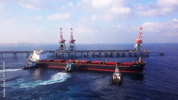 Obraz Large bulk carrier ship pulled by tugboats in open water