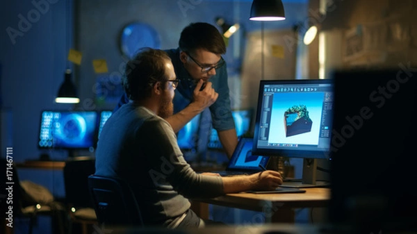 Fototapeta Dwóch projektantów gier płci męskiej omawia rysowanie poziomów gry, jeden używa tabletu graficznego. Pracują późno w nocy w biurze na poddaszu.