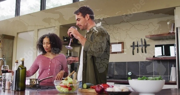 Fototapeta Couple cooking together stirring vegetables and sipping wine at kitchen island, with frying pan