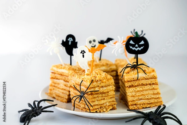 Fototapeta Slices of honey cake for a Halloween party, each adorned with fun and creepy toppers. Decorative black spiders creates a perfect mysterious and celebratory mood. Close-up. Selective focus.