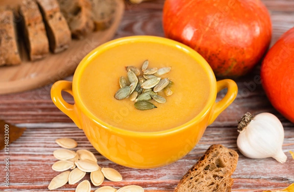 Fototapeta Delicious pumpkin cream soup and and crispy rye bread on a wooden table. Homemade food made from seasonal vegetables. Close-up. Selective focus.
