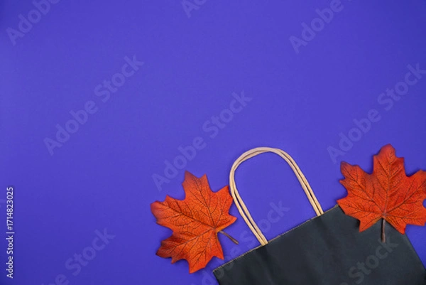 Fototapeta Black paper shopping bag and autumn leaves on an purple background. Autumn shopping and sales concept. Top view. Flatlay. Copy space.