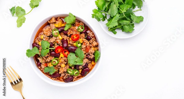 Fototapeta Spicy beef chili con carne with red beans, sweet corn, fresh cilantro, jalapeno pepper and tomato, served on white table, top view