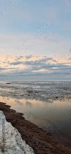Obraz Peaceful scene of ice floes drifting in calm ocean waters with stunning sunset sky. Reflective water surface captures colorful clouds, evoking serenity and tranquility. Vertical photo