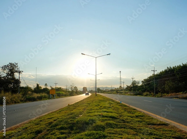 Fototapeta Evening wind powers turbines over a summer highway, connecting the city to the green rural landscape