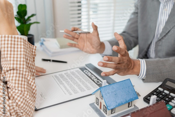 Fototapeta A real estate agent and client are discussing property purchase options, reviewing a contract, calculating loan terms, and considering house models as part of a housing investment decision.
