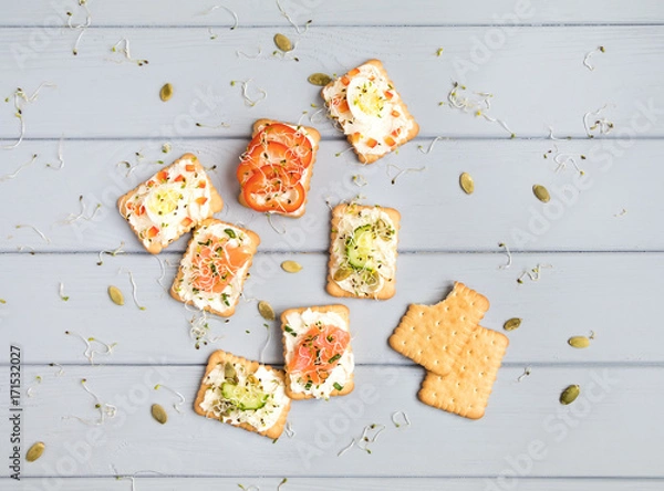 Fototapeta Crackers with cream cheese and various toppings. Appetizers on grey table. Healthy snacks, top view, flat lay