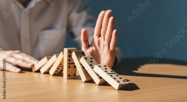 Fototapeta Hand stopping dominoes from falling, representing risk management and prevention