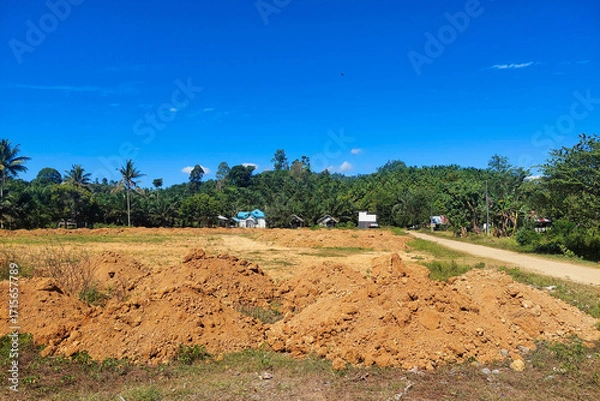 Fototapeta A football field under renovation with piles of soil and a clear blue sky in the background.