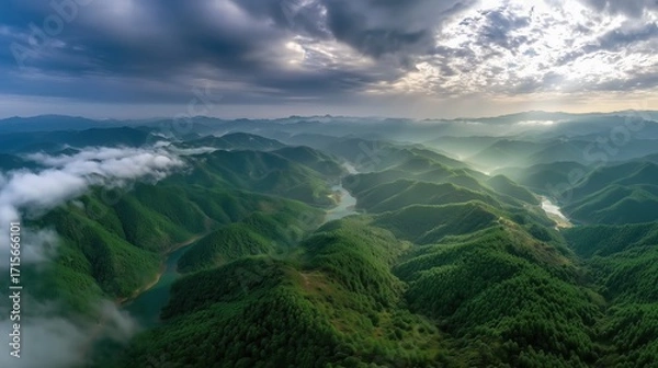 Fototapeta Aerial View of Lush Green Mountains Under Dramatic Cloudy Sky with Sunlight Rays
