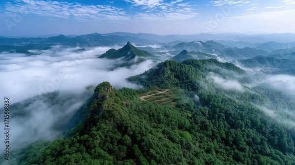 Fototapeta Aerial View of Lush Green Mountains Surrounded by Misty Clouds Under a Clear Blue Sky