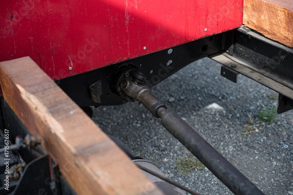 Fototapeta A detailed, close-up shot of the driveshaft and cardan joint on the undercarriage of a classic AA or BB truck with a wooden chassis.
