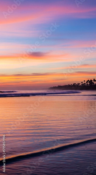 Fototapeta Vibrant sunset paints the sky with soft pinks and blues over a tranquil ocean and palm-lined coast