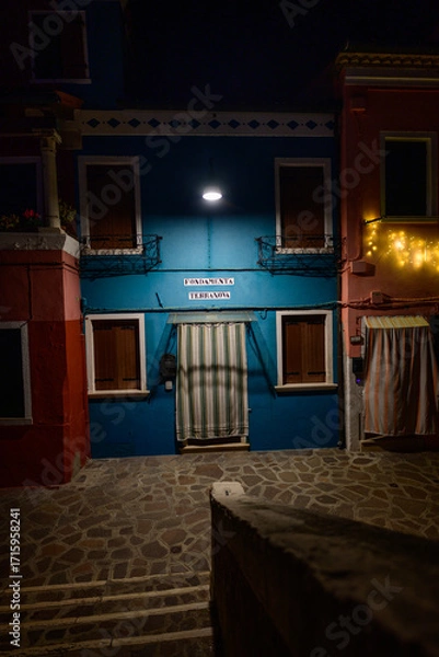 Obraz Burano, Italy - December 28 2025: Colorful Blue House Facade illumintade at Night on Fondamenta Terranova on Burano Island in the Lagoon of Venice.