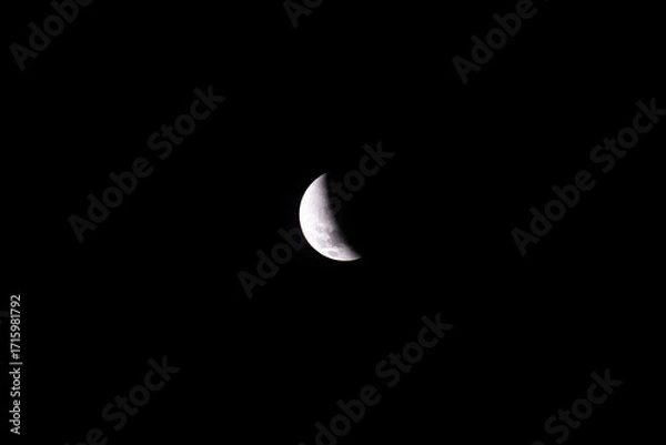 Fototapeta A breathtaking partial lunar eclipse reveals the Moon partially covered by Earth’s shadow, glowing softly against the deep, starless dark sky of a calm night.