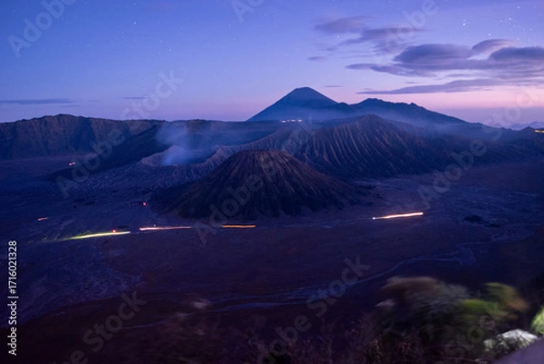Fototapeta Twilight view of Mount Bromo and surrounding Tengger caldera in East Java, Indonesia, with soft purple skies, misty volcanic slopes, and light trails glowing across the vast desert plain.