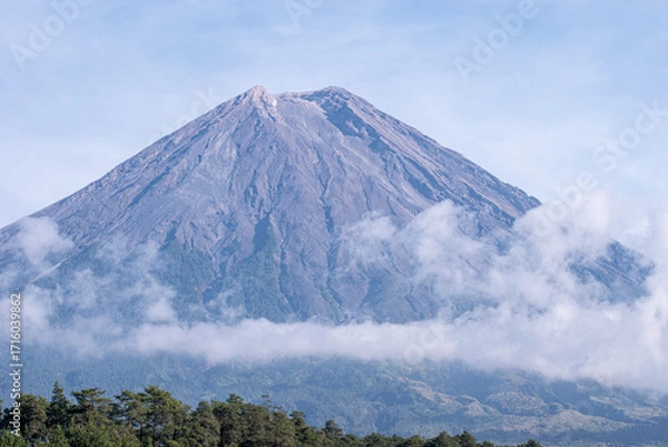 Fototapeta Mount Semeru’s iconic peak stands proudly against the expansive blue sky, its detailed volcanic ridges and textures clearly illuminated by daylight.