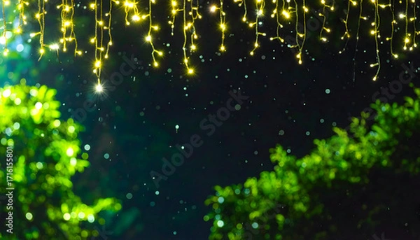 Fototapeta Twinkling yellow fairy lights illuminate a dark night sky with green trees and falling snow