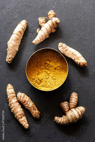 Fototapeta Fresh Turmeric Roots and Ground Powder on Dark Slate Background