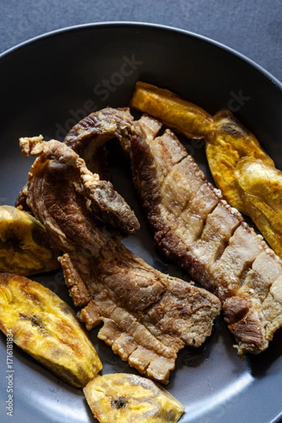 Fototapeta Crispy Fried Pork Belly with Fried Plantains on Dark Plate