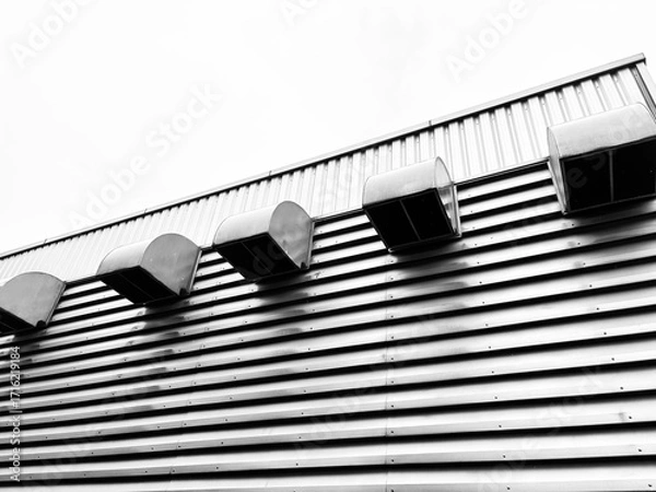 Fototapeta A close-up, low-angle shot of a building's corrugated metal wall, highlighting a series of industrial vents. The black and white photography emphasizes texture and modern, minimalist architecture.