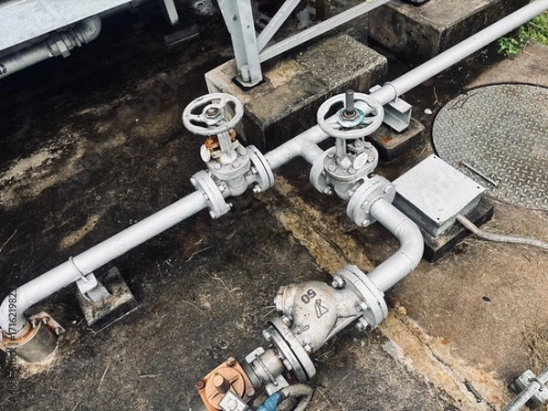 Fototapeta Industrial piping system with manual valves and flanges, set against a concrete background. This setup is typical for water, oil, or gas supply lines in a factory or refinery.