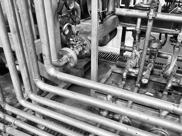 Fototapeta A striking black and white close-up of a complex network of industrial pipes, valves, and gauges. The image focuses on the intricate arrangement of metal tubes and machinery, highlighting the texture