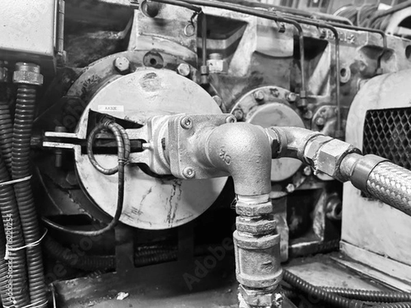 Fototapeta A detailed black and white close-up of complex industrial machinery. The image focuses on a collection of pipes, bolts, and metal components, highlighting the intricate engineering and robust construc