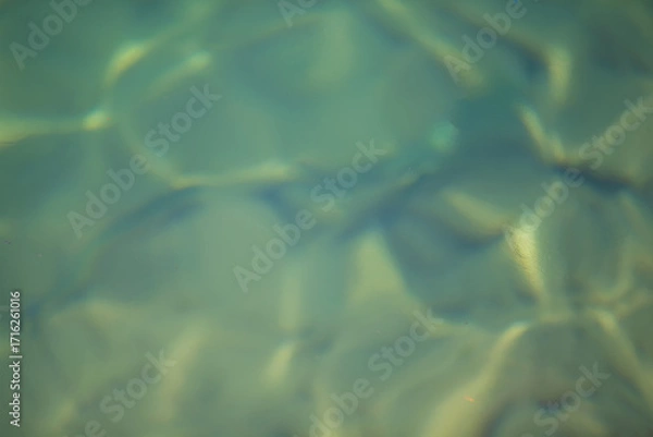Fototapeta A blurry image of water with a greenish tint. The water appears to be rippling and has a hazy quality