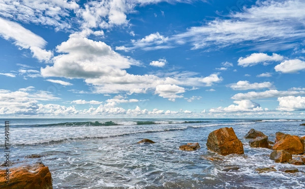 Fototapeta seascape featuring a stormy sea and fallen rock fragments, a horizon with cumulus clouds, a concept of turbulent elements and the power of nature, copy space for natural projects