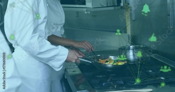 Fototapeta Cooking chefs wearing chef jackets stirring veggies in frying pan at gas range with network icons