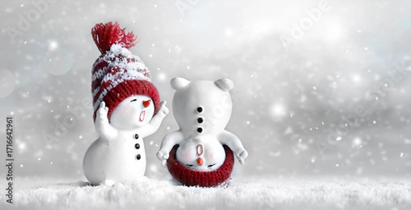 Fototapeta Two little snowmen in caps on snow in the winter. Background with a funny snowmen. Christmas card.