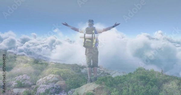 Fototapeta Standing hiker in shorts and boots extending arms toward clouds on mountain ridge with backpack mat
