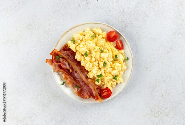 Fototapeta Scrambled eggs with crispy bacon and tomatoes on a white background. Classic breakfast.
