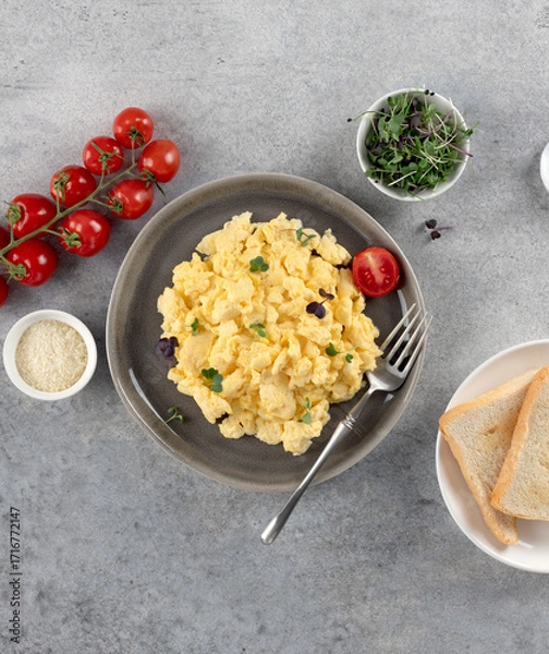 Fototapeta Scrambled eggs with microgreens, tomatoes, toast on grey background. Healthy breakfast. Top view.